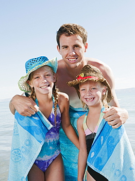 Portrait of girls (6-7,8-9) wrapped in towel on beach with their father