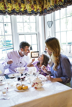 Parents and daughter (4-5) eating together in dining room