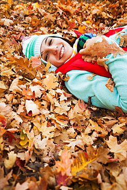 Portrait of smiling young woman lying on autumn leaves 