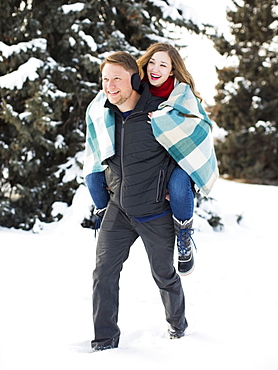 Man giving woman piggyback ride in winter forest, Salt Lake City, Utah