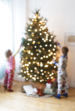 Sister and brother (4-5, 6-7) decorating christmas tree