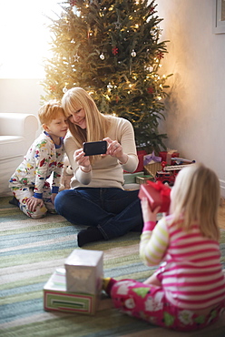 Mother with children (4-5, 6-7) opening christmas presents and taking photos