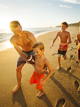 Father playing football on beach with his three sons (6-7, 10-11, 14-15), Laguna Beach, California