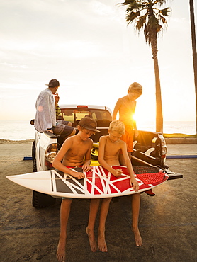 Boys (6-7, 10-11, 14-15) waxing surfboard at sunset, Laguna Beach, California