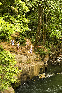 Women swinging on rope swing above river in distance, Costa Rica