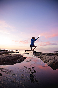 Teenage boy jumping between rocks of tide pool in La Jolla, California