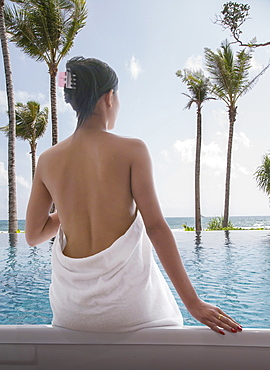 Woman wrapped in white towel sitting by swimming pool