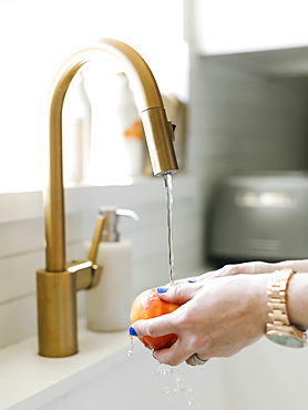 Hands of woman washing apple in kitchen sink