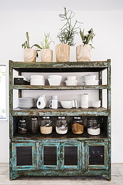 Worn shelves holding tableware, food and potted plants