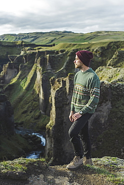 Young man standing on cliff above canyon in Kirkjubµjarklaustur, Iceland