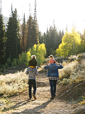 Two fathers piggybacking daughters while hiking