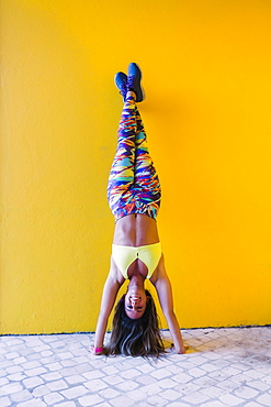 Smiling woman doing handstand by yellow wall