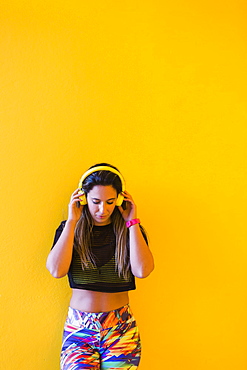 Woman wearing headphones by yellow wall