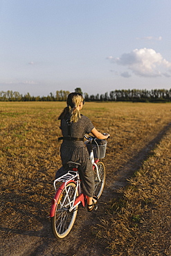 Woman riding bicycle in field, Belarus, Brest