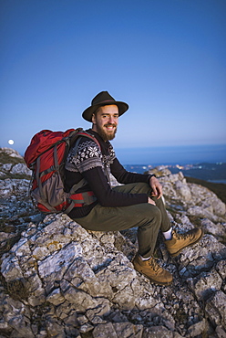 Smiling man sitting on rock at sunset