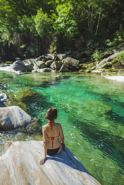 Woman wearing bikini sitting on rock by river