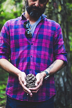 Man wearing checked shirt holding pinecone