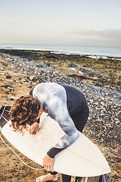 Teenage boy waxing surfboard at beach