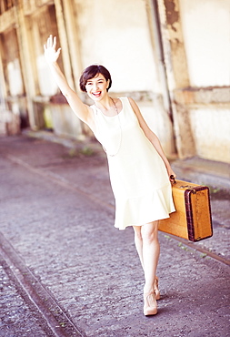 Woman in dress holding suitcase at train station, waving hand, USA, New Jersey, Jersey City 