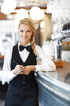 Portrait of smiling waitress standing by bar counter