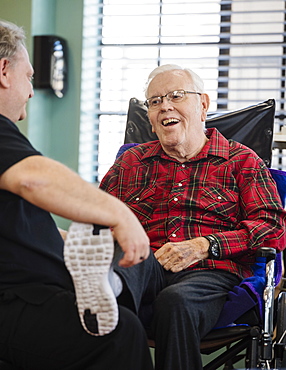 Nurse holding smiling senior man's foot in wheelchair