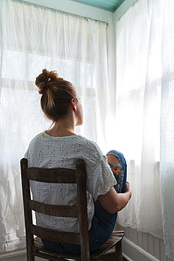 Woman sitting in front of curtained windows