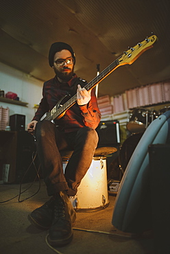 Young man playing bass guitar during rehearsal in garage