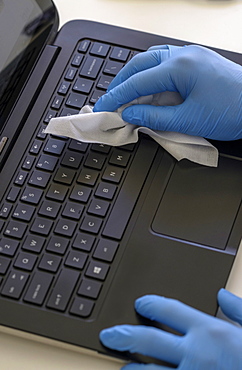 Person wearing blue surgical glove cleaning keyboard of laptop