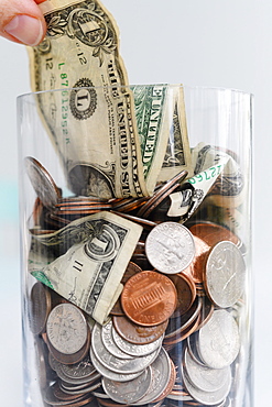 Close-up of fingers pulling one dollar bill from jar with American cents and banknotes