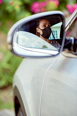 Woman with face mask driving car reflected in mirror
