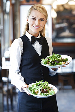 Portrait of young waitress holding plates with salad