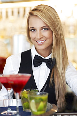 Portrait of female bartender holding tray with cocktails