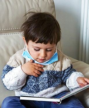 Boy (2-3) wearing face mask holding book