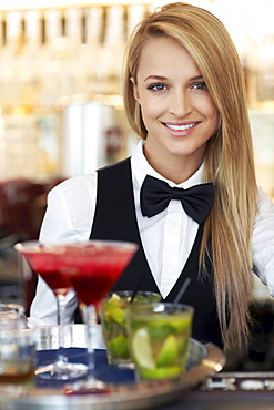 Portrait of female bartender holding tray with cocktails