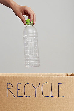 Close up of boys (8-9) hand putting plastic bottle into cardboard box