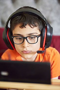 Boy (8-9) gaming on tablet while sitting in bed during weekend