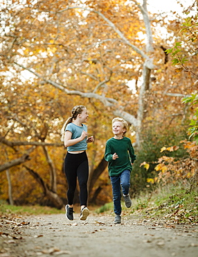 United States, California, Mission Viejo, Boy (10-11) and girl (12-13) running on footpath in forest