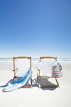 Empty beach chairs with bag and towel on beach