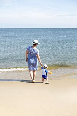 Mother and young son, holding hands, walking on beach, rear view