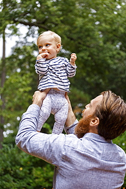 Father holding baby girl in air, outdoors