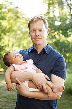 Father outdoors holding baby girl looking at camera smiling