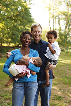 Family outdoors posing for photograph holding preschool boy and baby girl looking at camera smiling