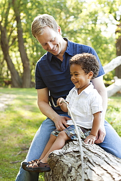 Father and son sitting on log holding twig smiling