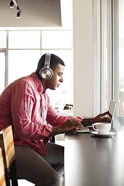 Young man in coffee shop, wearing headphones, using laptop