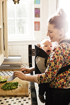 Mid adult mother preparing food with baby son in sling