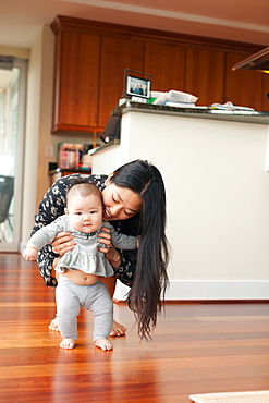 Mother supporting baby girl to walk