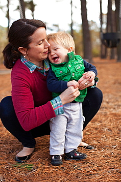 Laughing mother tickling son in park