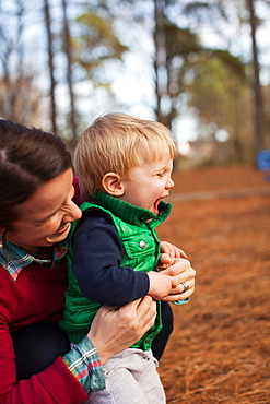 Laughing mother tickling son in park