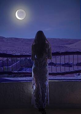 Dubai, United Arab Emirates, Woman in luxury resort in desert watching moon and starry sky at night