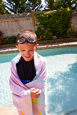 Smiling boy (8-9) wrapped in towel standing on poolside